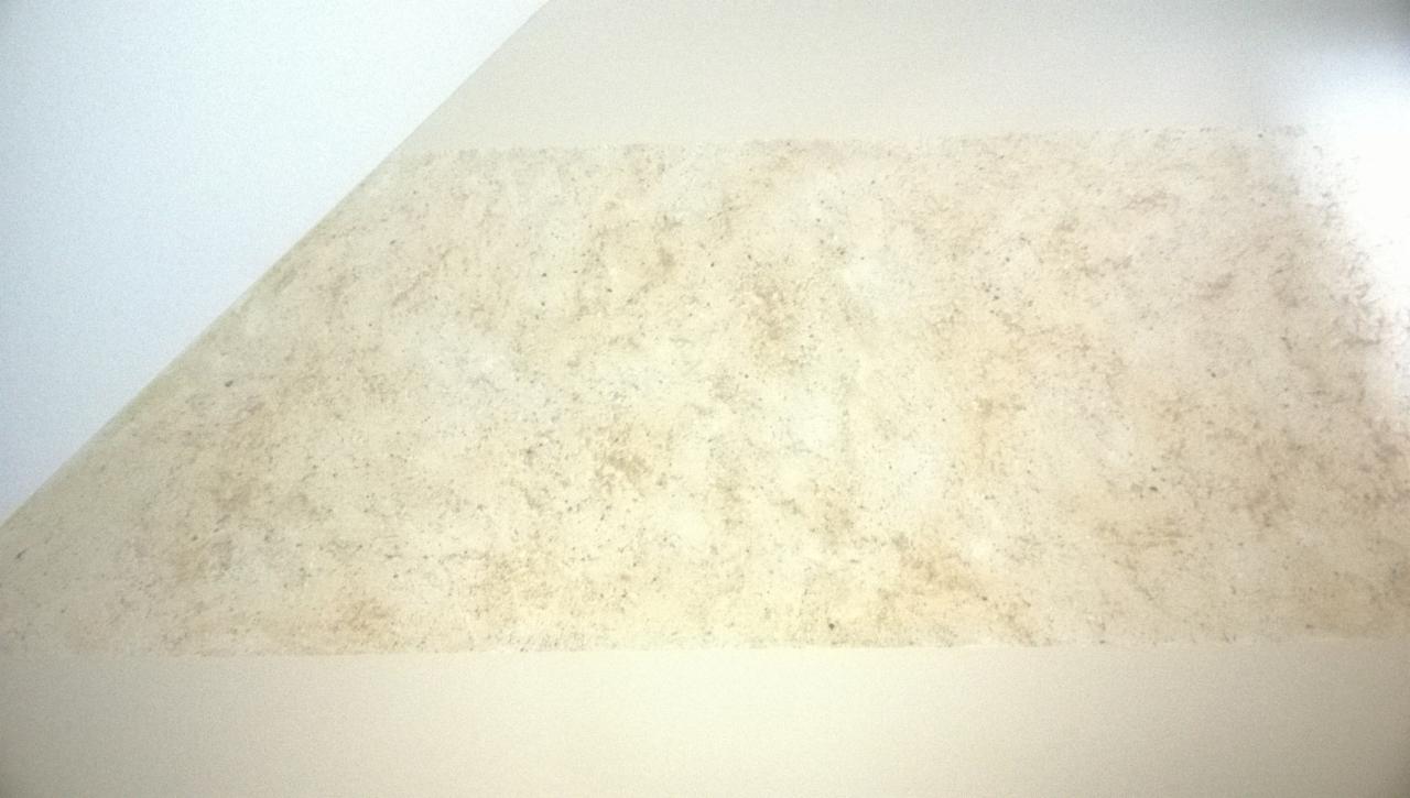 Fragment ściany wykończonej dekoracyjną, beżową strukturą, widoczny pod skosem, z gładkim, białym fragmentem sufitu u góry.