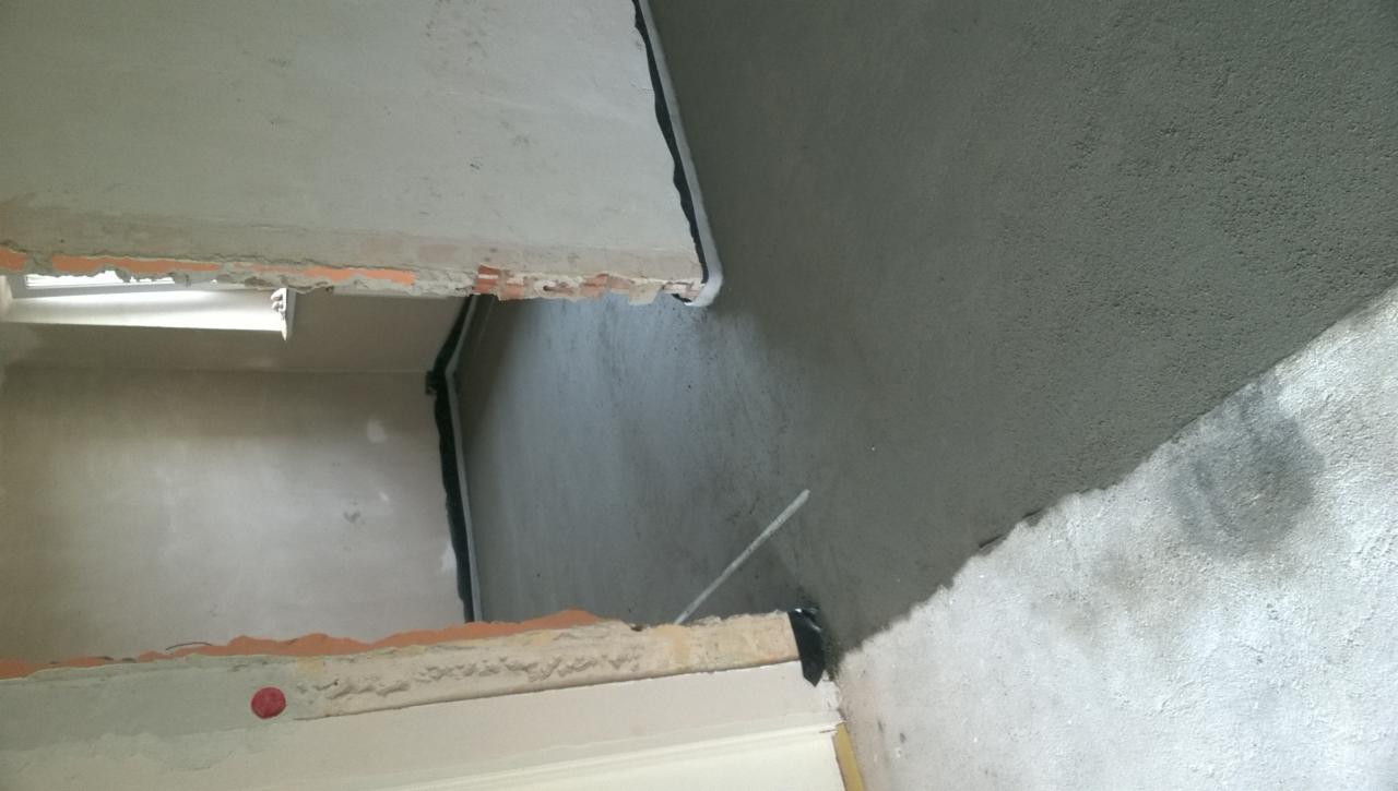 Przygotowanie podłoża pod gładzie: surowy tynk cementowo-wapienny na ścianie, widoczne fragmenty cegieł i wystające przewody elektryczne.