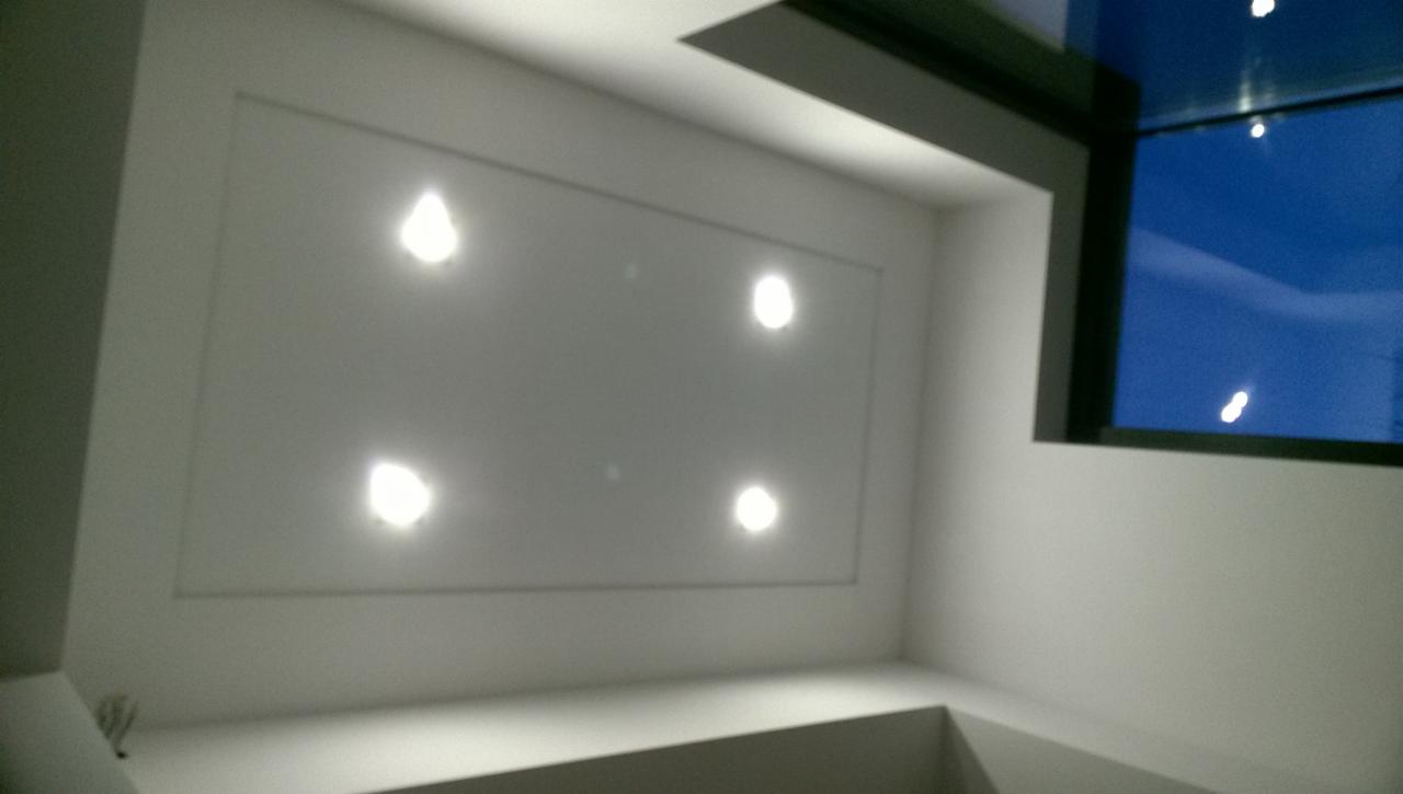 Biały sufit podwieszany z wbudowanymi czterema punktowymi lampami LED, widok z dołu, fragment okna z ciemną ramą