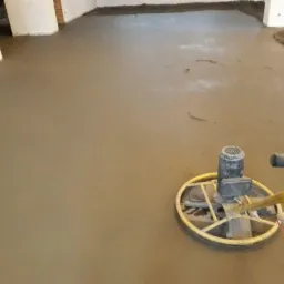 Zacieranie świeżo wylanego jastrychu mechaniczną zacieraczką na tle surowych ścian i kolumn w pomieszczeniu.