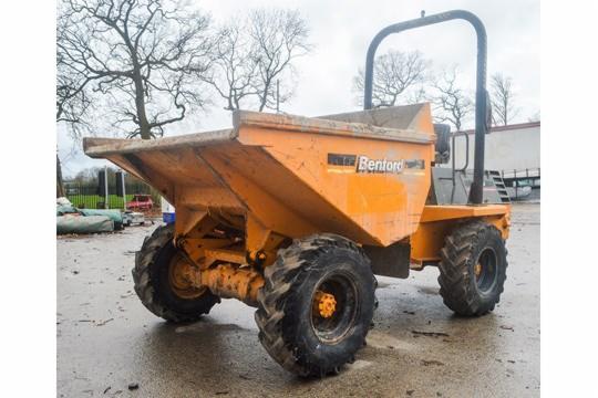 Pomarańczowa wywrotka budowlana Benford z dużymi oponami na mokrym placu, widoczne drzewa w tle.