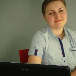 Kobieta w bluzce w paski siedzi przed laptopem Sony na czerwonym krześle, spoglądając w obiektyw z lekkim uśmiechem. Szare tło.