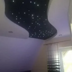 Czarny, podwieszany sufit w kształcie nieregularnej łzy z białymi punktami świetlnymi imitującymi gwiazdy, widok z dołu w pokoju z żelazkiem na desce do prasowania.