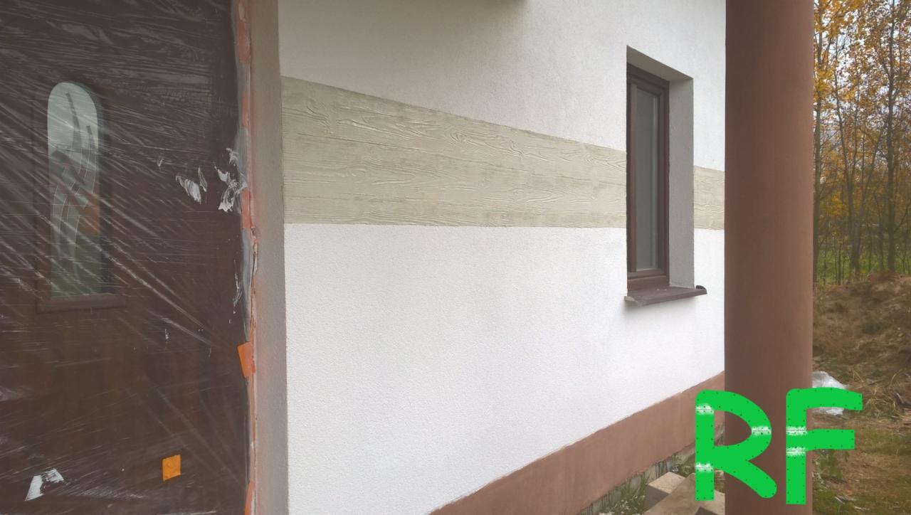 Fragment elewacji budynku z poziomym pasem dekoracyjnym imitującym drewno, okno z brązową ramą i brązowa kolumna. Drzwi wejściowe zabezpieczone folią ochronną.