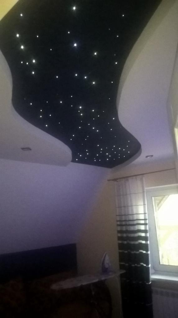 Czarny, podwieszany sufit w kształcie nieregularnej łzy z białymi punktami świetlnymi imitującymi gwiazdy, widok z dołu w pokoju z żelazkiem na desce do prasowania.