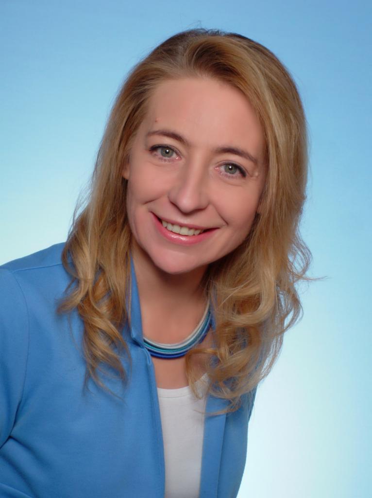 Portret uśmiechniętej kobiety w niebieskiej marynarce i naszyjniku z niebieskich koralików na jasnoniebieskim tle.