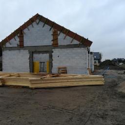 Rafał Wojda - Surowy stan domu z betonu komórkowego z drewnianą konstrukcją dachu w trakcie budowy, widoczne przygotowane elementy więźby dachowej, na placu budowy stoi betoniarka.