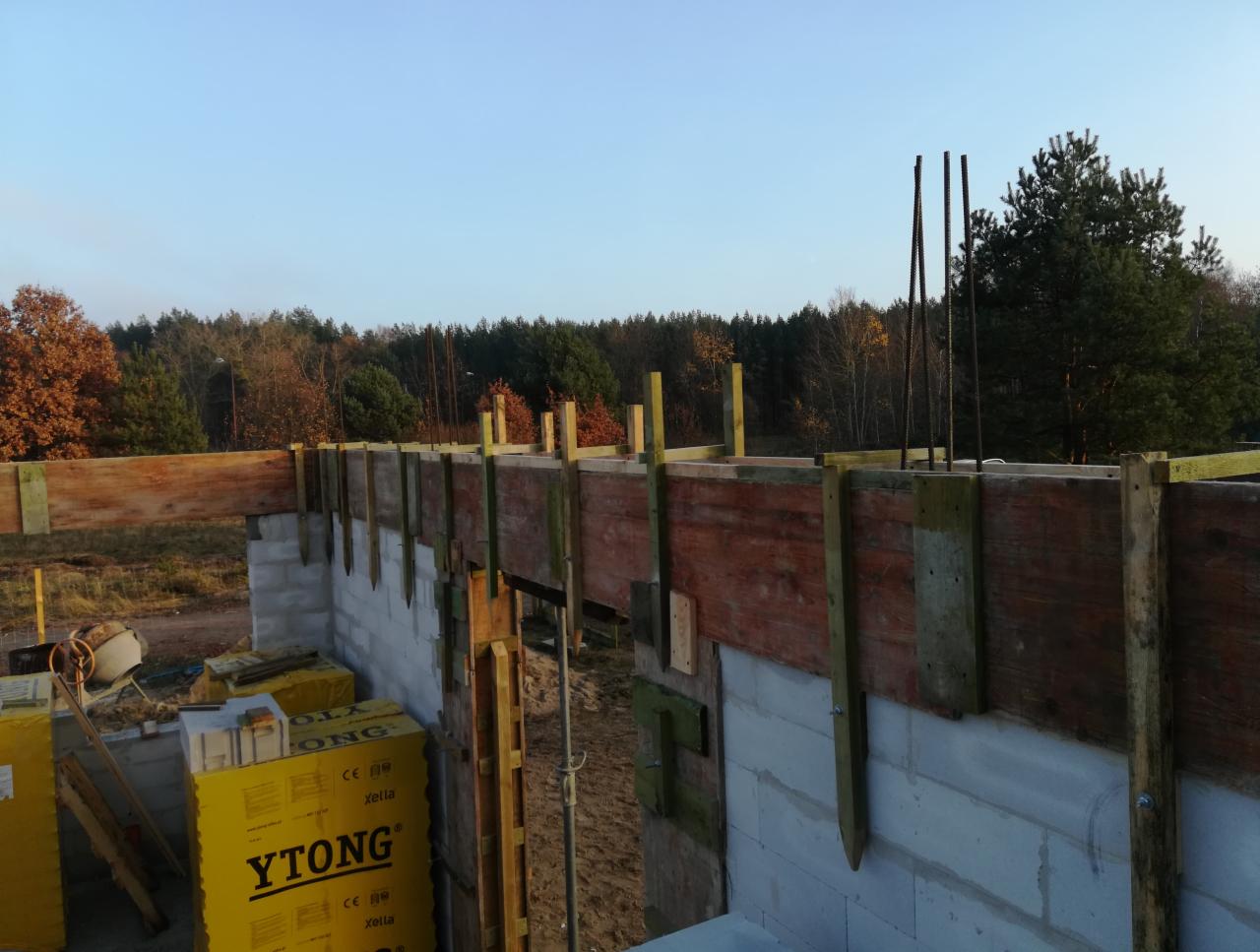 Wznoszenie ścian z bloczków Ytong na fundamencie, widoczne szalunki i zbrojenie, w tle las i błękitne niebo.