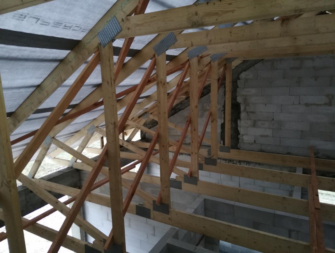 Konstrukcja drewniana dachu w trakcie budowy domu z bloczków, widoczne krokwie, łaty i membrana dachowa.