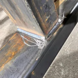 Spoina łącząca metalowe profile pod kątem, widoczne ślady rdzy i niedoskonałości spoiny, ukazujące surowy charakter obróbki metalu.