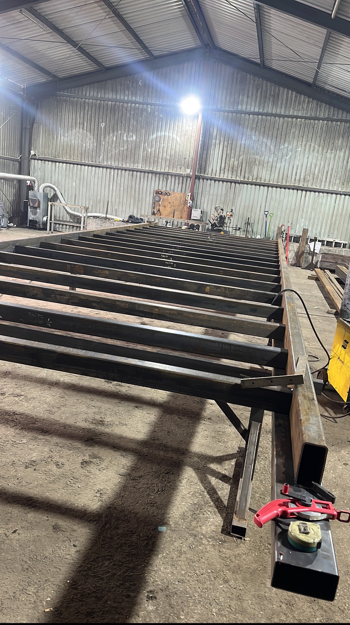 Konstrukcja stalowa w hali produkcyjnej: spawane profile tworzą szkielet, z narzędziami obok. Widoczne detale montażu i surowe oświetlenie.