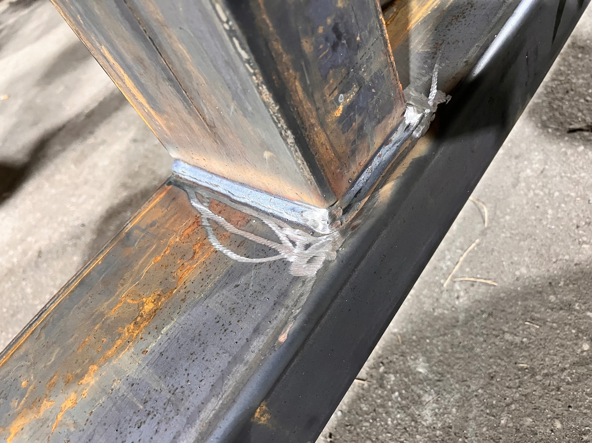 Spoina łącząca metalowe profile pod kątem, widoczne ślady rdzy i niedoskonałości spoiny, ukazujące surowy charakter obróbki metalu.