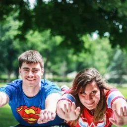 Para w kostiumach Supermana i Wonder Woman pozuje, leżąc na ławce w parku, udając lot.