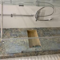 MAGGROUP Sp. z o.o. - Nowoczesna kabina prysznicowa z deszczownicą i baterią podtynkową, wykończona płytkami w odcieniach beżu i błękitu, z widocznym drewnianym elementem wykończeniowym.