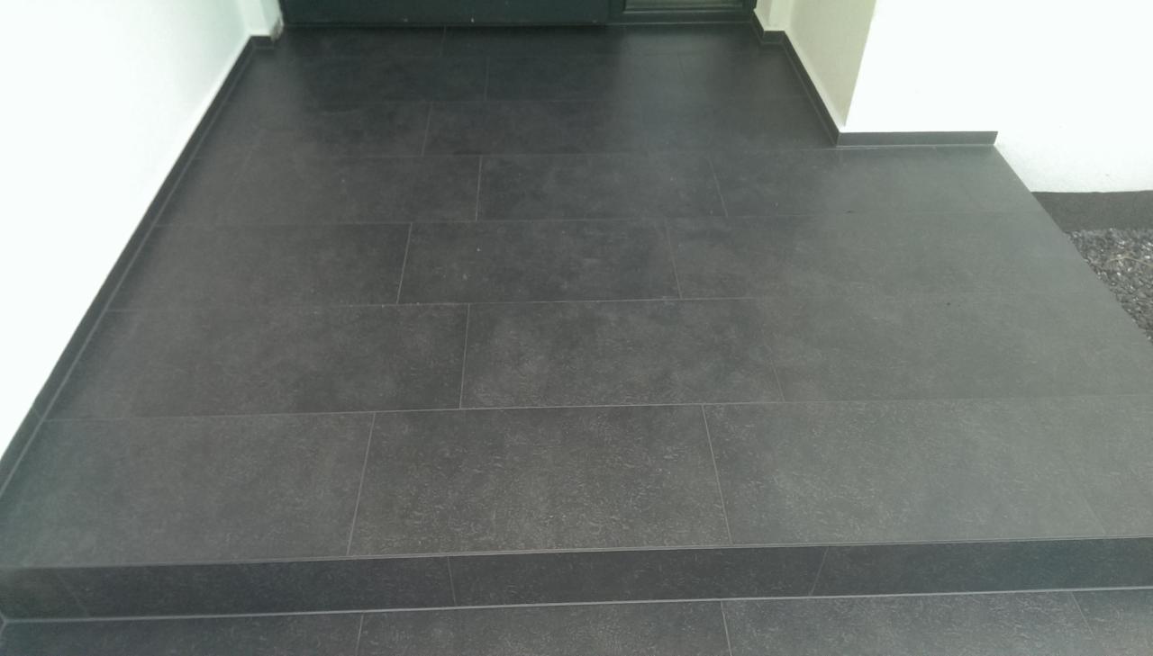 Nowoczesne, ciemnoszare płytki gresowe ułożone na schodach wejściowych do budynku, z widoczną fugą i fragmentem białej ściany.