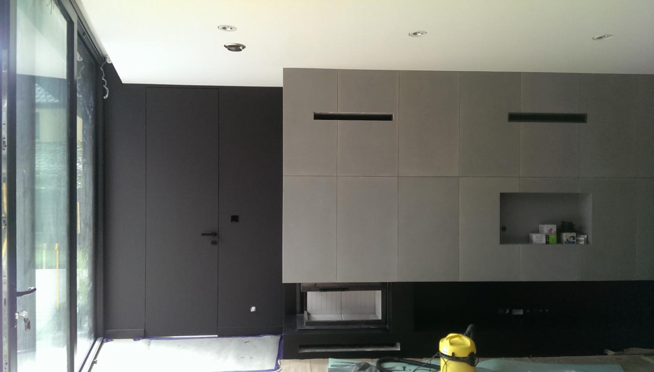 Nowoczesne wnętrze z szarą zabudową ściany, w której znajduje się kominek; widoczny odkurzacz i resztki materiałów budowlanych.