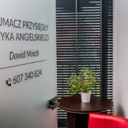 Szklane drzwi z napisem 'Tłumacz Przysięgły Języka Angielskiego Dawid Mnich' i numerem telefonu, widok na wnętrze biura z żaluzjami, stolikiem i rośliną doniczkową.