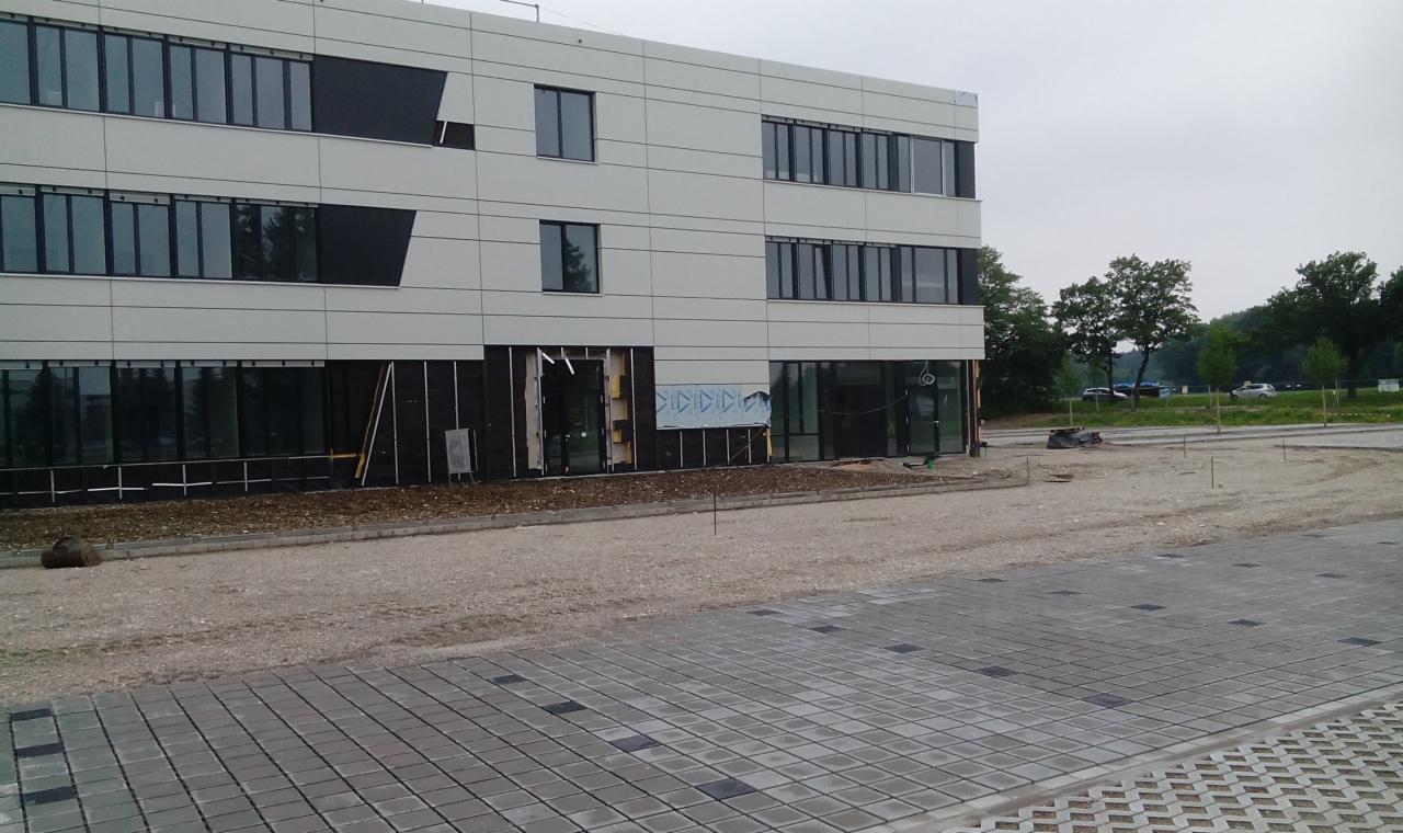 Budynek biurowy w trakcie prac elewacyjnych, widoczne odsłonięte fragmenty ścian, rusztowania i przygotowany teren wokół.