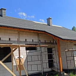 Probud - Budynek w trakcie budowy z widocznym dachem pokrytym papą, rusztowaniami i pustakami ceramicznymi, na tle błękitnego nieba.