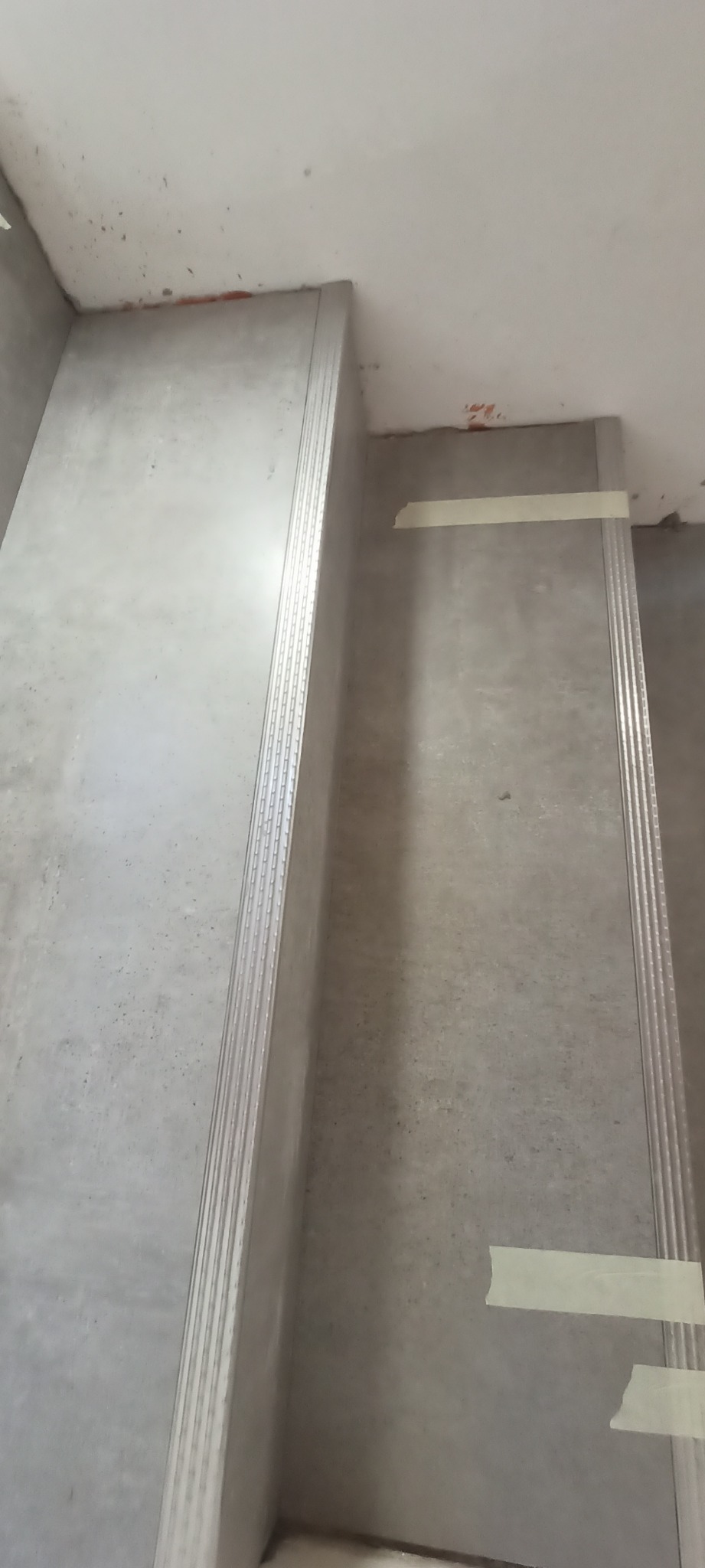 Montaż płyt gipsowo-kartonowych na schodach, widoczne profile i taśma malarska zabezpieczająca powierzchnię.