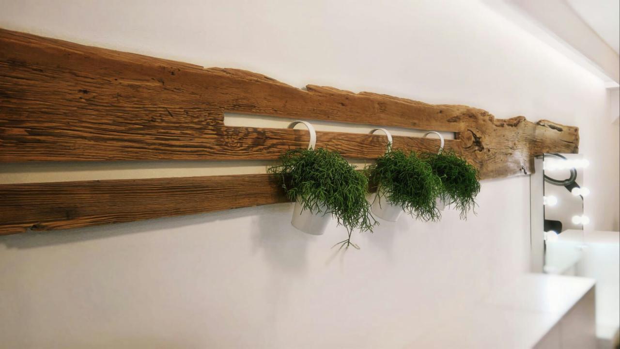 Dekoracyjny drewniany panel ścienny z trzema wiszącymi doniczkami z zielonymi roślinami, oświetlona toaletka z lustrem w tle.