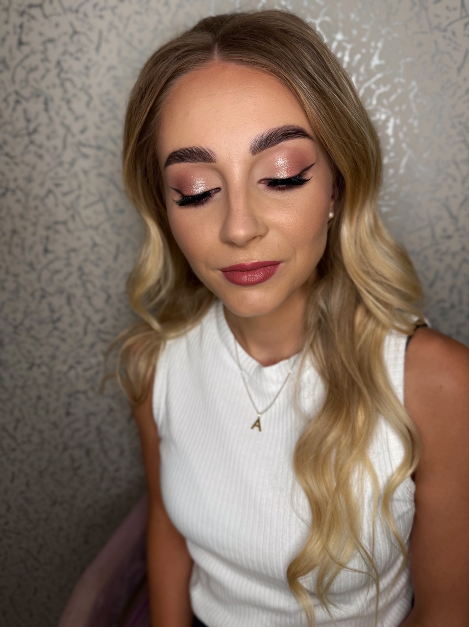 Blondynka z zamkniętymi oczami prezentuje delikatny, błyszczący makijaż oka z czarną kreską i podkreślone brwi. Usta w kolorze mauve. Tło w neutralnej tonacji.