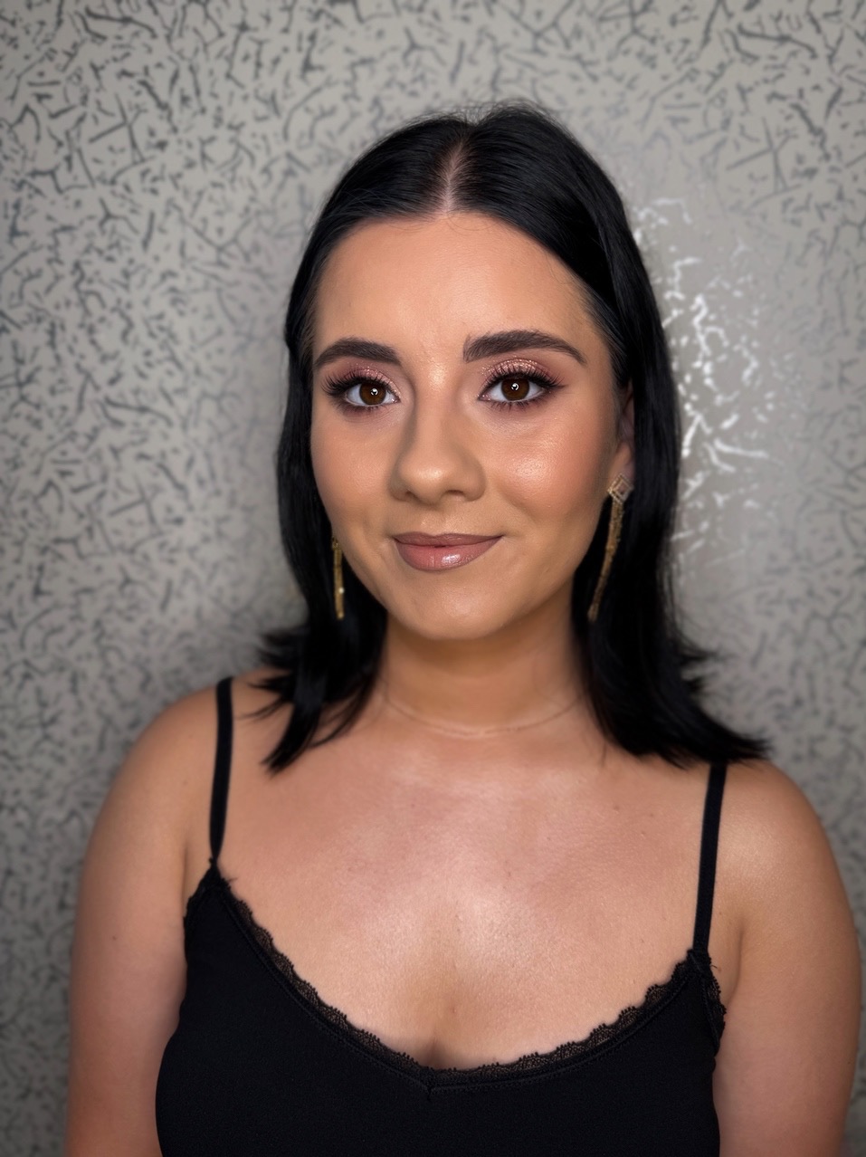 Portret kobiety z profesjonalnym makijażem: podkreślone oczy w odcieniach brązu, błyszczące usta, delikatny kontur twarzy i złote kolczyki.