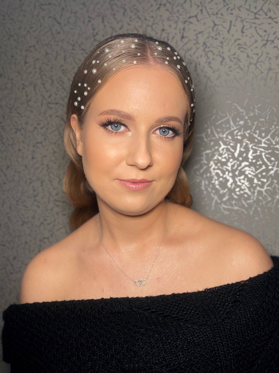 Portret kobiety z delikatnym upięciem włosów zdobionych perłami i subtelnym wizażem, wykonanym w Męcinie. Uwagę przyciągają długie rzęsy i rozświetlona cera.