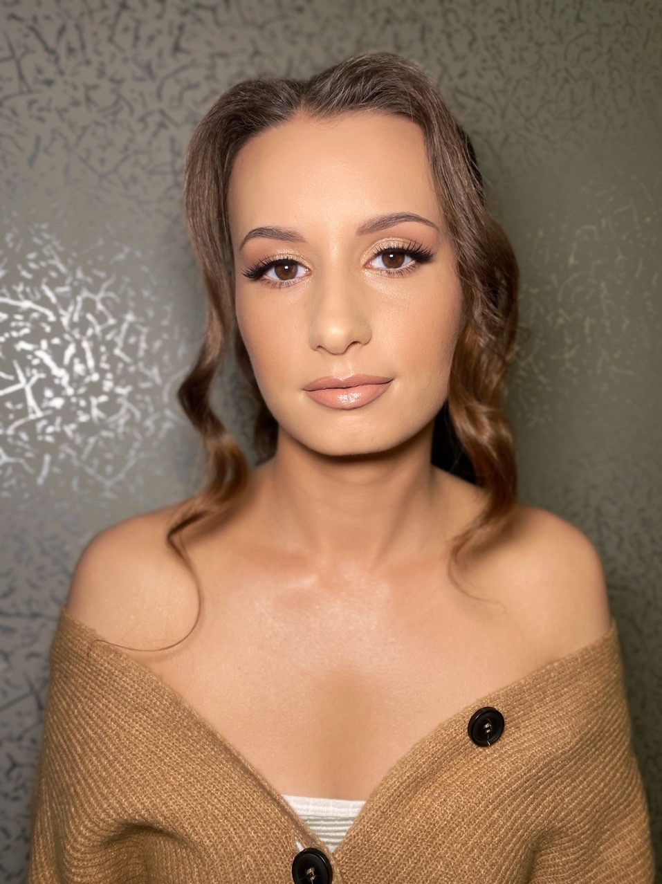 Portret kobiety z subtelnym makijażem, podkreślone oczy i usta w odcieniach nude, brązowe, delikatnie falowane włosy, beżowy sweter.