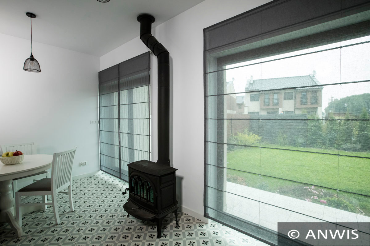 Nowoczesne wnętrze z szarymi roletami rzymskimi, piecem wolnostojącym i wzorzystą podłogą.