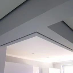 Szare podwieszane elementy sufitowe tworzące geometryczny wzór nad wejściem do pomieszczenia, z widocznymi punktowymi źródłami światła w białej części sufitu.