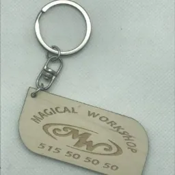 Drewniany brelok z wygrawerowanym logo 'Magical Workshop' i numerem telefonu, przymocowany do metalowego kółka.