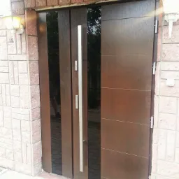 Nowoczesne, brązowe skrzydło z pionowymi przeszkleniami, umieszczone w ceglanej elewacji z zewnętrznymi lampami.