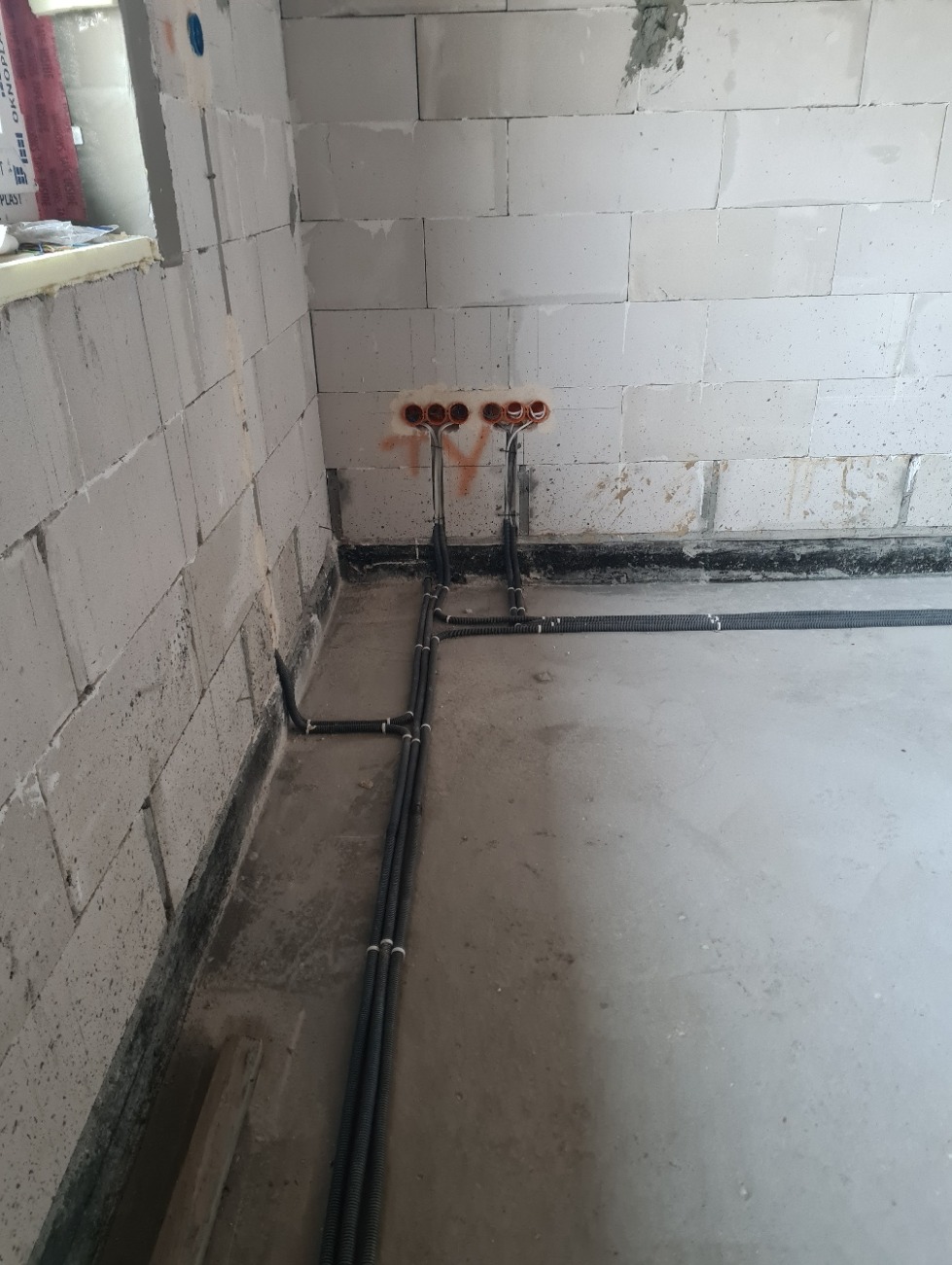 Surowy stan: Instalacja elektryczna w peszlach na ścianie z betonu komórkowego, widoczne puszki pod gniazdka i przewody prowadzone po podłodze.