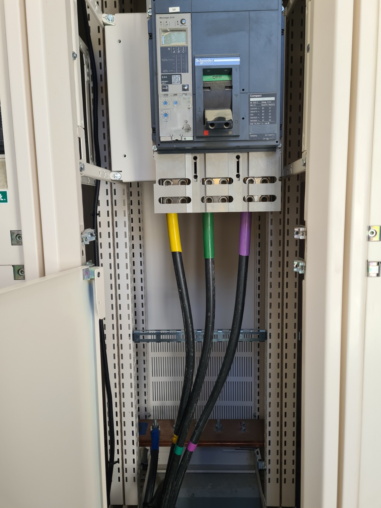 Rozdzielnica elektryczna z widocznymi, kolorowymi kablami (żółty, zielony, fioletowy) podłączonymi do wyłącznika Schneider Electric, widoczne oznaczenia napięć i prądów na urządzeniu.