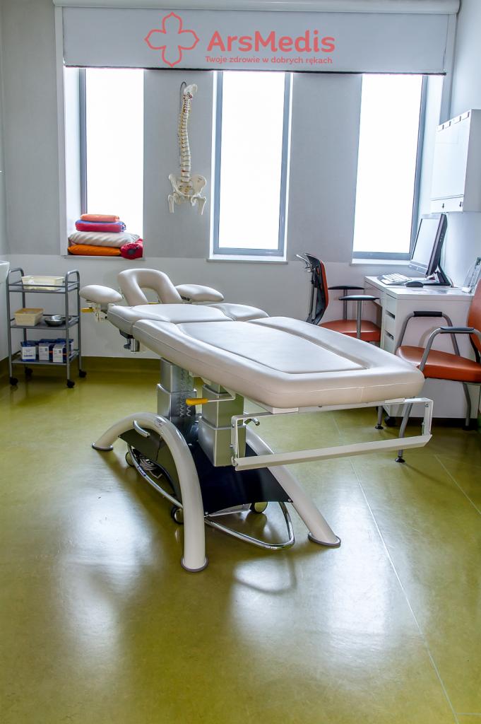 Jasny gabinet z regulowanym stołem do masażu, szkieletem kręgosłupa na ścianie i logo ArsMedis nad oknem.