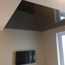 Pomieszczenie po malowaniu: beżowe ściany, ciemnoszary sufit z oknem dachowym i zamontowany telewizor.