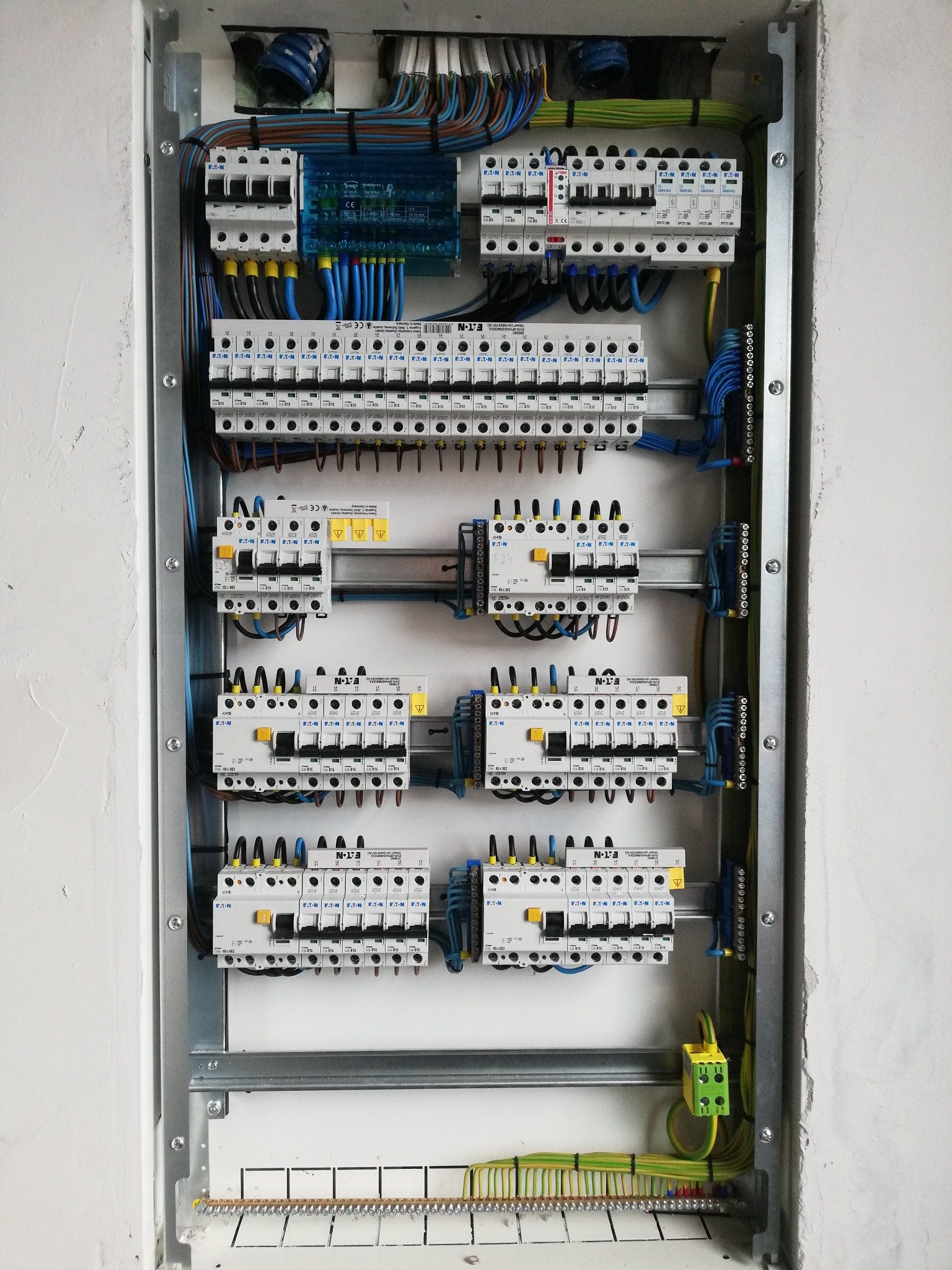 Rozdzielnica elektryczna z zainstalowanymi bezpiecznikami i okablowaniem, widok z bliska na szarej ramie montażowej.