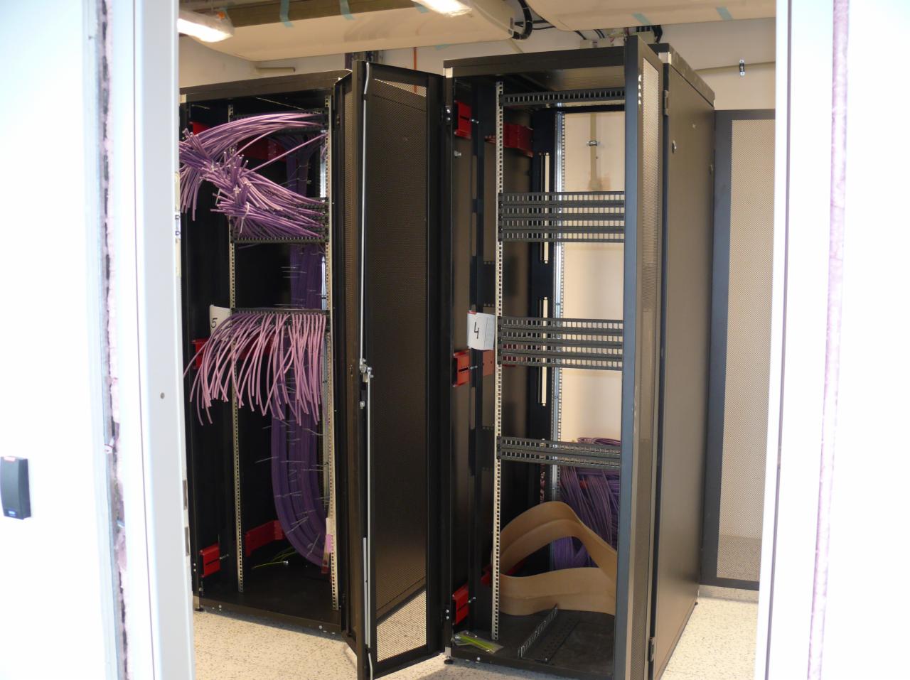 Dwa otwarte serwery rack z fioletowymi kablami, widoczne numery '4' i '5' na czerwonych uchwytach, uporządkowane okablowanie w szafach serwerowych.