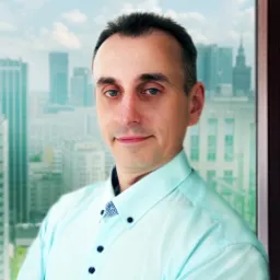 Portret mężczyzny w błękitnej koszuli na tle panoramy miasta z wieżowcami, widocznej przez okno.