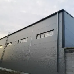 Szary budynek przemysłowy z płyt warstwowych, widok z dołu, z widoczną konstrukcją z betonu komórkowego w narożniku.