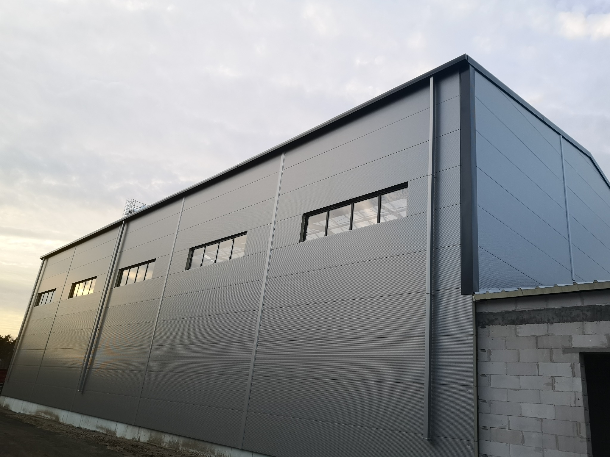 Szary budynek przemysłowy z płyt warstwowych, widok z dołu, z widoczną konstrukcją z betonu komórkowego w narożniku.