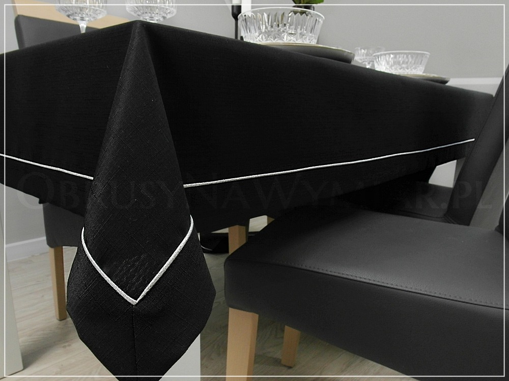 Elegancki, czarny obrus z białą lamówką na stole z zastawą, krzesła w tle. Klasyczny design z dbałością o detale.