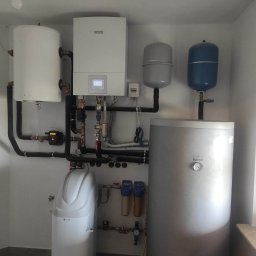 AKWA SOLAR BOLESŁAW KOPEĆ SP.J. - Kompletna instalacja grzewcza w kotłowni: biały wiszący kocioł gazowy Bosch z wyświetlaczem, zbiornik buforowy Galmet, dwa zbiorniki wyrównawcze, zmiękczacz wody USTM oraz liczne rury i zawory.