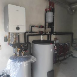 AKWA SOLAR BOLESŁAW KOPEĆ SP.J. - Nowoczesna instalacja grzewcza z piecem gazowym marki Bosch, dwoma zbiornikami akumulacyjnymi, rurami z czarnymi izolacjami i zaworami, widoczne przewody wentylacyjne pod sufitem.