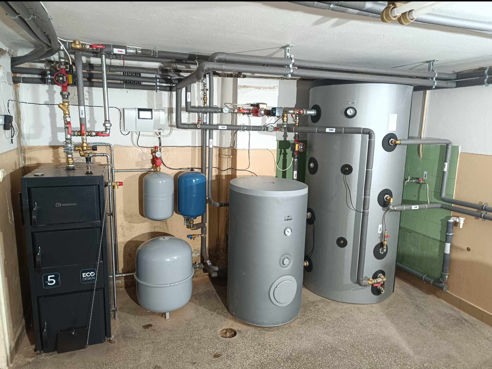 Zainstalowany system grzewczy w piwnicy: kocioł zasypowy marki Kamen z oznaczeniem Eco Design, dwa zbiorniki buforowe c.o. oraz zasobnik c.w.u. z licznymi rurami i zaworami.