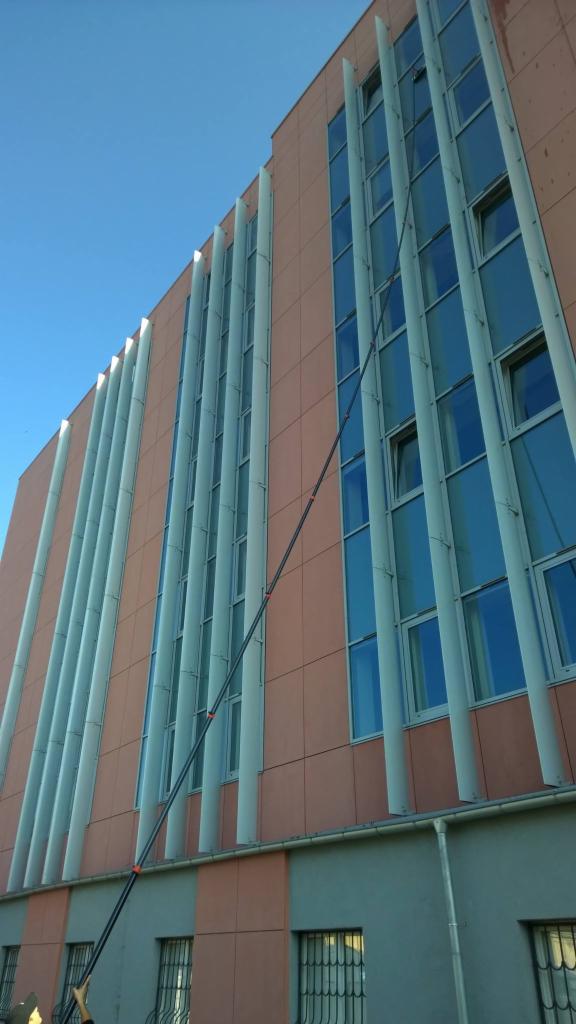 Mycie okien na wysokości za pomocą teleskopowej lancy na tle budynku biurowego z kolumnami.