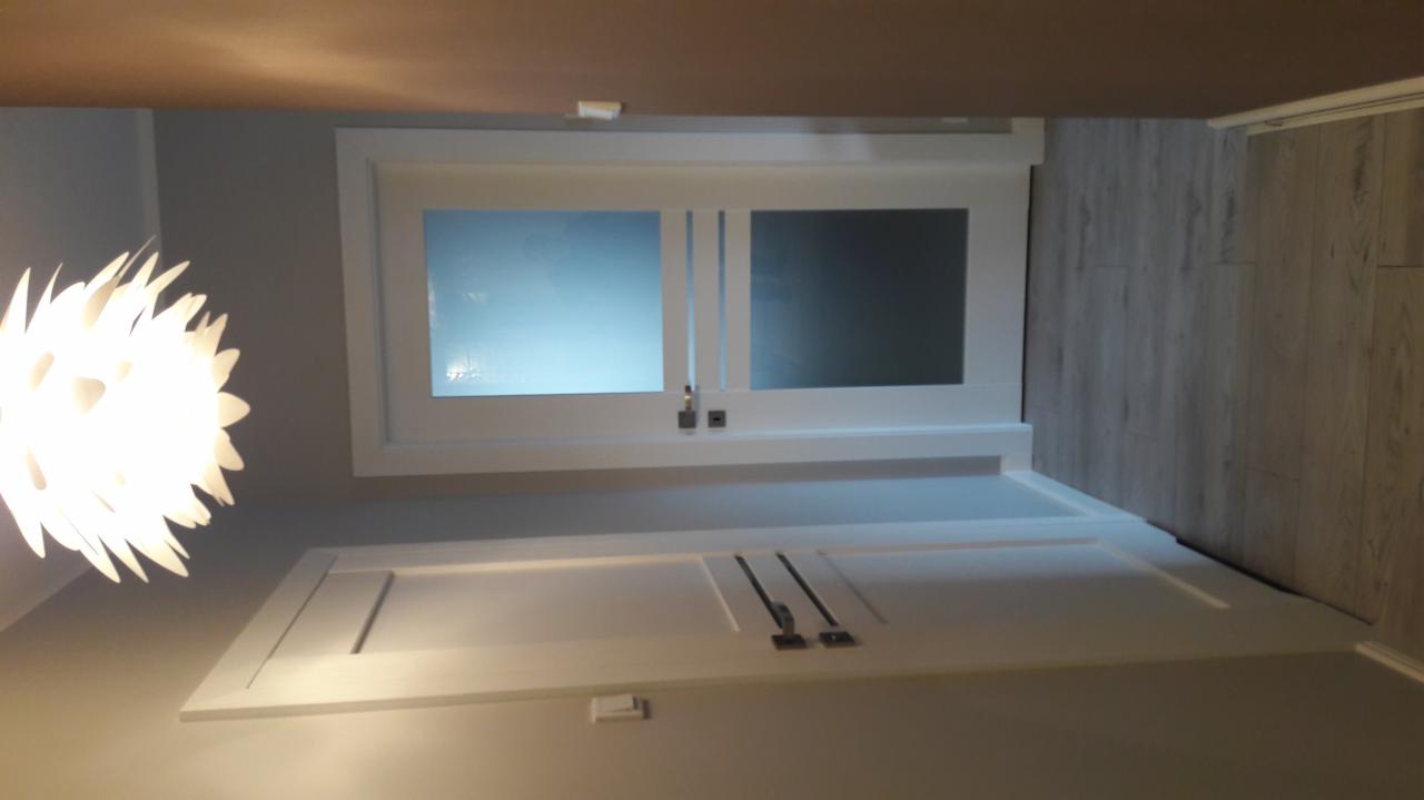 Białe, dwuskrzydłowe drzwi przesuwne z matowym szkłem, zamontowane w nowoczesnym wnętrzu z panelami podłogowymi i designerską lampą.