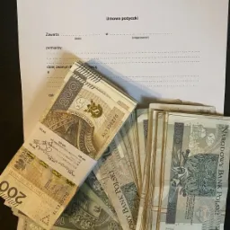 Stos banknotów 100 i 200 złotych leżący na formularzu umowy pożyczki z pustymi polami do wypełnienia.