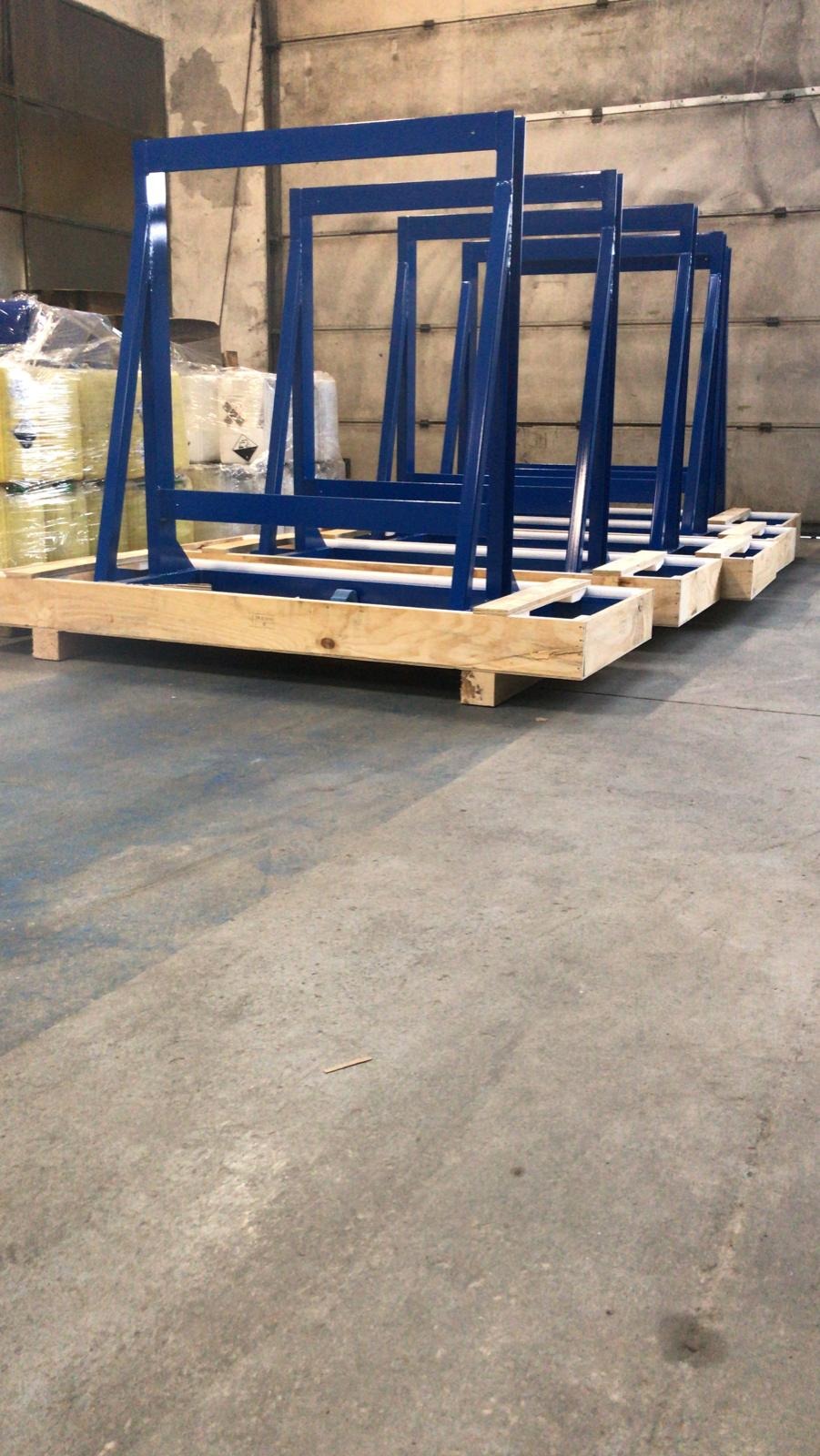 Rząd niebieskich, metalowych stojaków na paletach w magazynie, z zapakowanymi materiałami w tle.